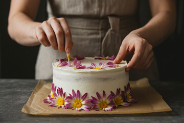 careful hands decorating vegan cake with organic flower petals, healthy dessert finishing