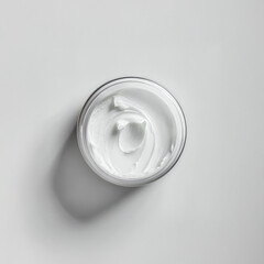 Minimalist top view of open skincare cream jar on white background.