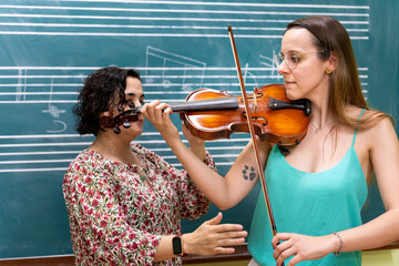 Music teacher helping student playing violin in front of blackboard with musical notes