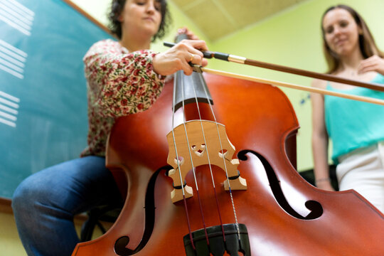 Music teacher playing double bass with student watching in class