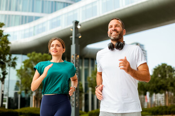 Fototapeta premium Joyful couple enjoying a morning jog through a modern urban landscape with inspiring architecture and greenery surrounding them