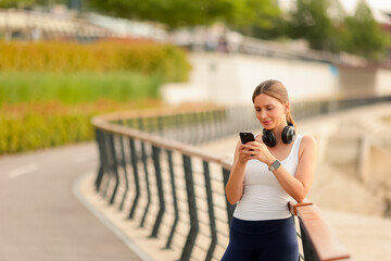 Enjoying a sunny afternoon, a woman listens to music while checking her phone by the waterside...