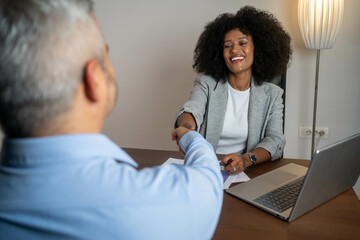 Happy mid aged business woman manager handshaking greeting client in office. Smiling female executive making successful deal with partner shaking hand at work at meeting table. 