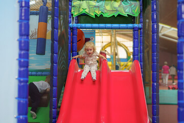 Child plays on a colorful slide in an indoor playground during afternoon fun time with friends
