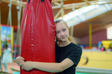 Young girl embraces a red punching bag while practicing in a gym during a training session