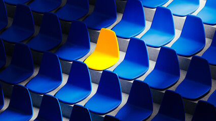 Bright yellow stadium seat stands out among blue chairs in isolation