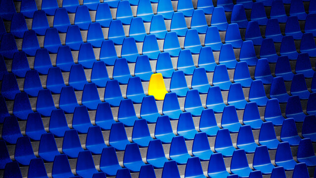 Bright yellow stadium seat stands out among blue chairs in isolation