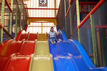 Colorful indoor playground features a girl sliding down bright slides in the afternoon