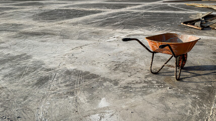 Old rusty construction wheelbarrow on an empty dusty concrete site. Industrial minimalism concept...