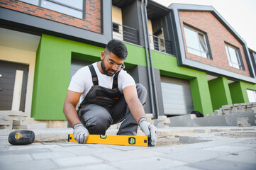 Indian master in gloves lays paving stones in layers. Garden brick pathway paving by professional...