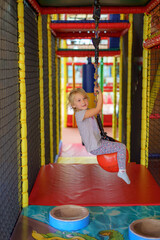 Young girl enjoys swinging on a colorful playground zip line at an indoor play area during afternoon fun time
