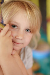 Young child with blonde hair smiling while holding onto a colorful structure in a playful environment