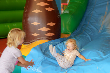 Children play joyfully on inflatable slide at indoor playground during sunny afternoon