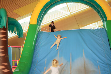 Children enjoy sliding down a large inflatable structure in a brightly lit indoor play area during a fun recreational day