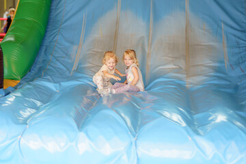Two young children enjoying themselves on a large inflatable slide during a fun event at an indoor play center