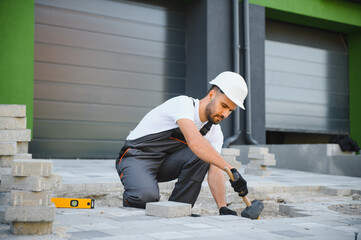 Worker skillfully laying paving stones using a hammer and wearing gloves, showcasing precision