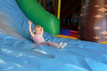 Young girl joyfully sliding down a colorful inflatable slide at an indoor play center