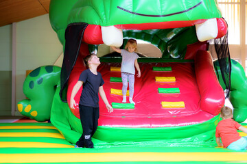 Children enjoy playing on a large inflatable dinosaur in a gym during a weekend afternoon