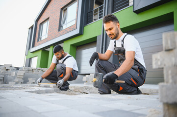 Two workers are laying paving stones near the house