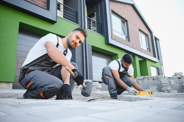Two workers are laying paving stones near the house