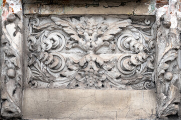 A detailed decorative relief carving on a wall, intricate floral and scroll motifs. Capturing the beauty of historic craftsmanship with an aged and weathered charm, the artistry of the past.