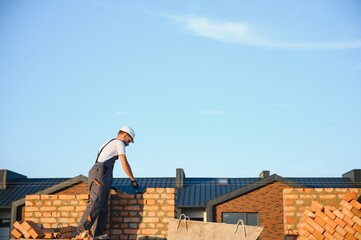 construction mason worker bricklayer installing red brick with trowel putty knife outdoors