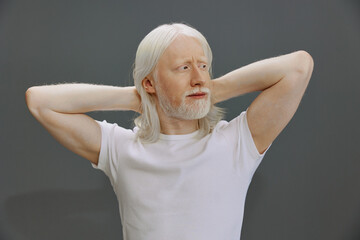 Portrait of a mature man with long white hair and a beard, relaxing with arms behind his head,...