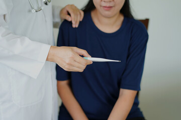 Professional asian young woman doctor is holding a oral digital thermometer, taking a sick...