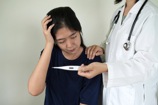 Professional asian young woman doctor is holding a oral digital thermometer, taking a sick patient's temperature at the hospital or clinic, ensuring accurate and hygienic temperature readings.