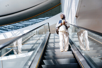Muslim woman going down escalator with smoothie