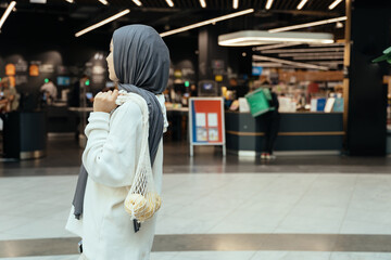 Conscious shopper in hijab checking eco bag with fruit