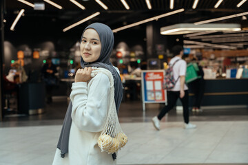 Conscious shopper in hijab checking eco bag with fruit