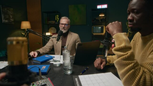 POV rack focus of podcast recording team having interview with male mature guest sitting at table in cozy studio