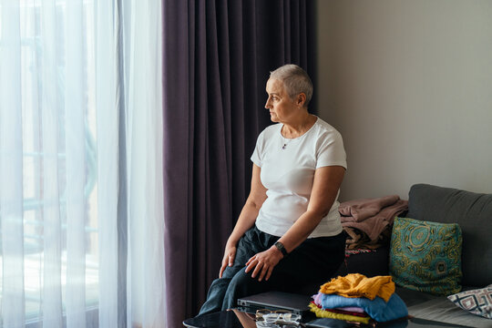 Middle-aged woman in white t-shirt gazing through window at home