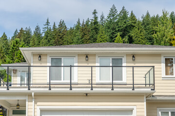 Top of grey stucco luxury house with shingle roof, green trees and nice windows in Spring in Vancouver, Canada, North America. Day time on May 2025.