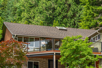 Top of grey stucco luxury house with shingle roof, green trees and nice windows in Spring in Vancouver, Canada, North America. Day time on May 2025.