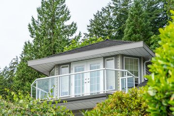 Top of grey stucco luxury house with shingle roof, green trees and nice windows in Spring in Vancouver, Canada, North America. Day time on May 2025.