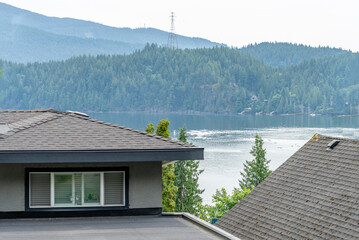 Top of grey stucco luxury house with shingle roof, green trees and nice windows in Spring in...