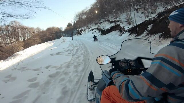 Person navigates a snowmobile up a snowy trail on a sunny winter day