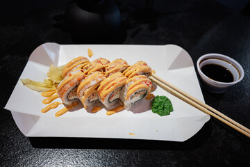 Delicious sushi roll with sauce served on a paper tray with chopsticks