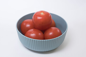 Close-up of five ripe tomatoes in a light green container, on a white background.