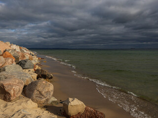 Sea. Seashore, huge rocks, sand, small waves of water and a dark cloudy sky are visible