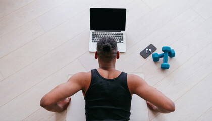 Training At Home. Sporty man doing the training while watching an online tutorial on a laptop, exercising in the living room, free space.