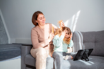 Woman braids a girl's hair. Happy Caucasian mother and sweet little daughter spend time together at...