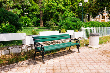 Green wooden bench in sunny park. Public space, relaxation area, and outdoor urban furniture