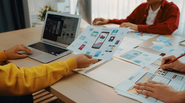 Excellent startup company employee presenting user interface prototype for mobile application to smart co-worker in office workspace. UX UI designer explain function of icon design on paper. Synergic