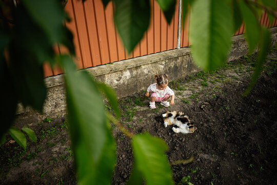 Child sitting outdoors playing with a cat amidst garden foliage