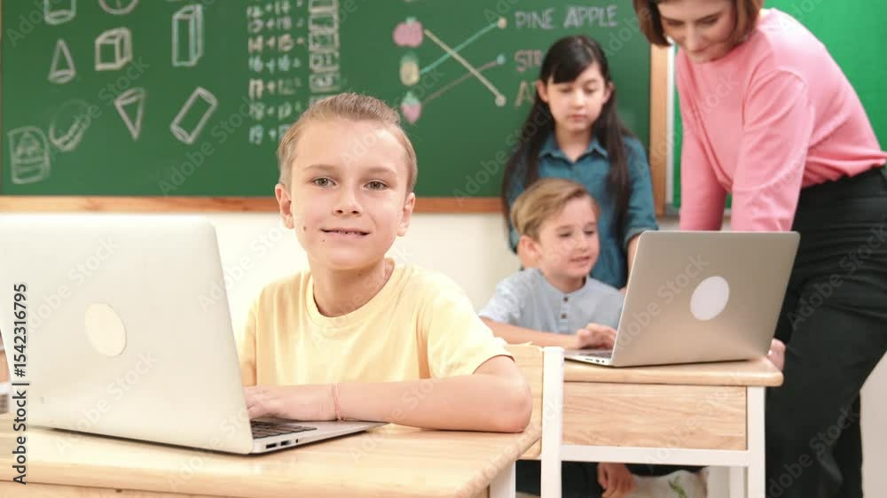 Poster caucasian boy focus on programing system while looking at camera surrounded by diverse student codin