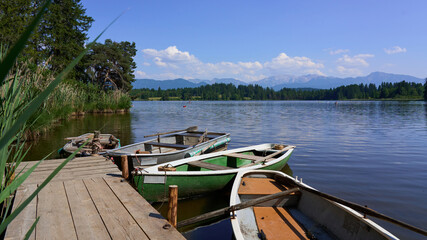 Rowboats docked on a calm alpine lake with a wooden pier and scenic mountain range in the...