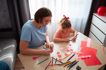 Wide shot of young Caucasian woman and a cute little girl are painting together sitting at a table....